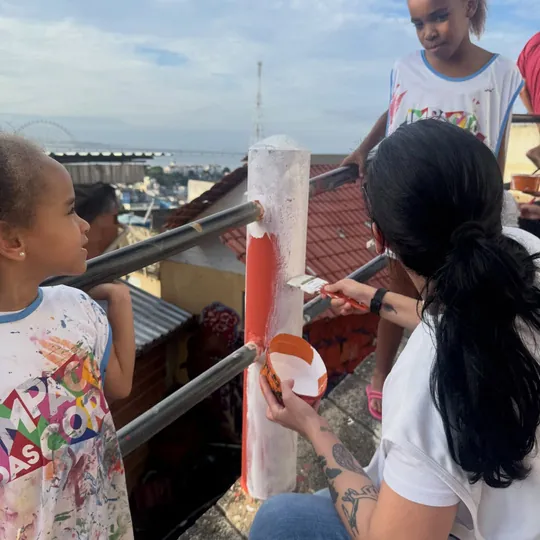 Voluntária pinta uma estrutura ao lado de crianças.